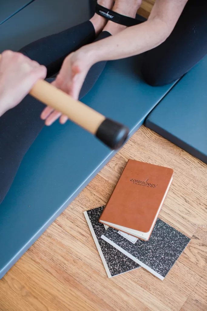 Two people engage in a workout with one person holding a bar and another sitting on a blue mat. In the foreground, there is a brown Controversy journal placed on top of two black-and-white speckled notebooks on a wooden floor, capturing the scene as only a San Diego Branding Photographer could.