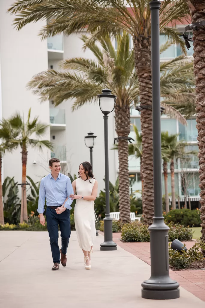 couple holding hands in front of the Southpointe hotel del coronado in san diego. white dress and blue button-down with navy pants