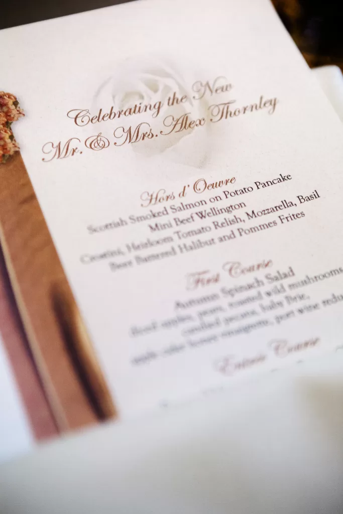 A close-up image of a wedding reception menu. The text reads "Celebrating the New Mr. & Mrs. Alex Thornley" at the top. It includes sections for Hors d'Oeuvre, First Course, and Second Course, listing various gourmet dishes such as smoked salmon and beef Wellington.